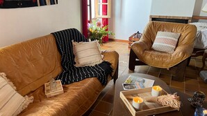 Ein Wohnzimmer mit einem braunen Ledersofa, einem Ledersessel, einem Couchtisch mit Zeitschriften, Kerzen und einer Ablage mit Dekoration.