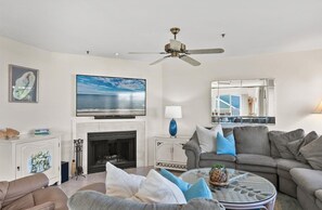 A living room with a fireplace, a ceiling fan, a large TV, and a sofa with cushions. - Beautiful Ocean Block home with fantastic views and a Hot Tub! (DEWEY BEACH)