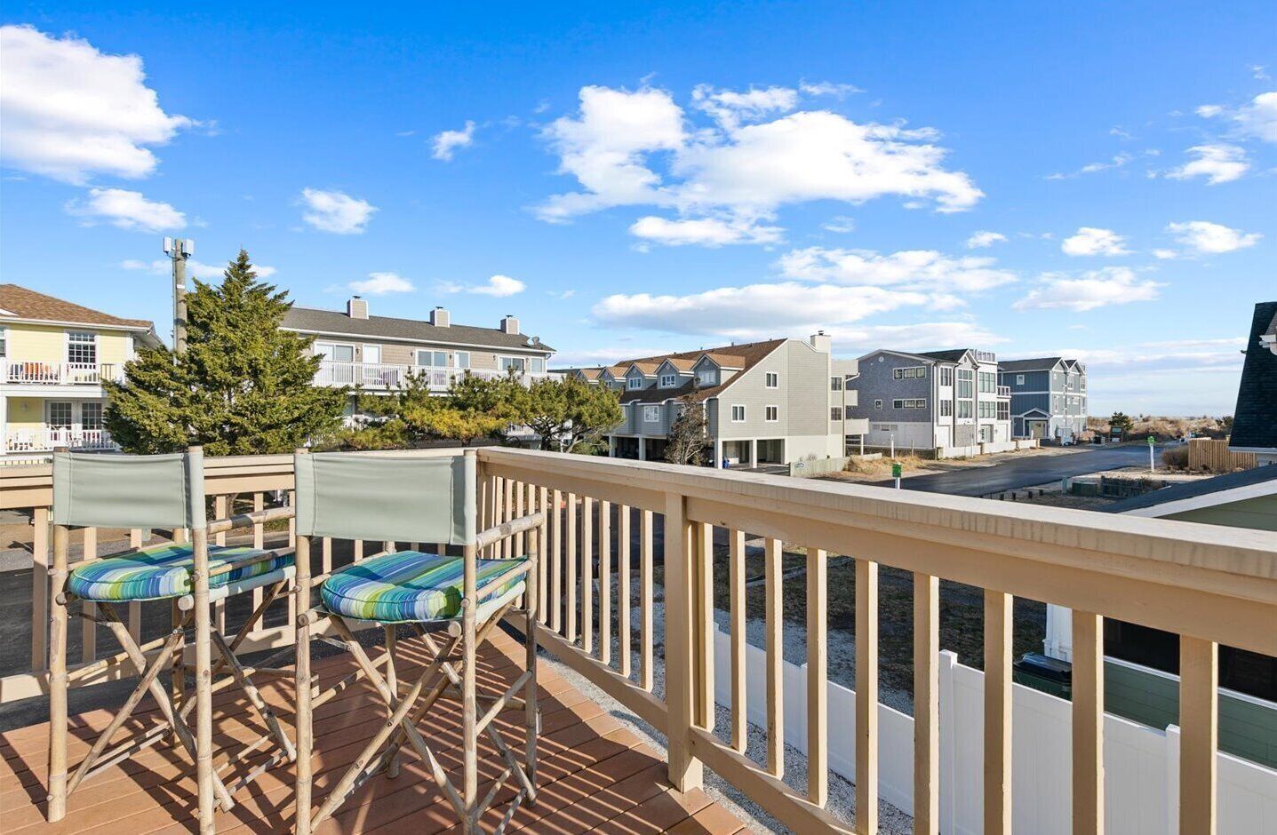 A balcony with a view of residential buildings, a wooden railing, and two chairs with cushions.