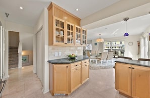 A modern kitchen with wooden cabinets, a central island, and a dining area with chairs and a table. - Beautiful Ocean Block home with fantastic views and a Hot Tub! (DEWEY BEACH)