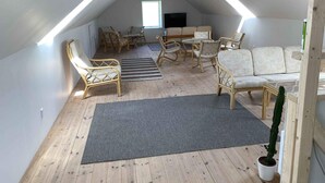 A loft-style room with a sloped ceiling, wooden beams, a sofa, chairs, a small table, and a potted plant. - 4 Star Holiday Home in Orsted (Ørsted)