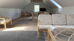 An attic room with a sloped ceiling, wooden beams, a sofa, chairs, a glass coffee table, and a window. - 4 Star Holiday Home in Orsted (Ørsted)