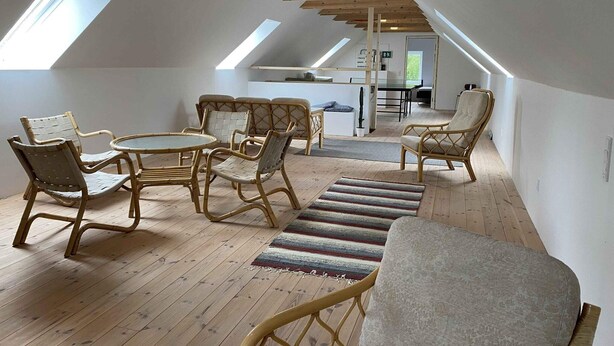 A loft-style room with a sloped ceiling, wooden beams, a dining table with chairs, a sofa, and a striped rug. - 4 Star Holiday Home in Orsted (Ørsted)