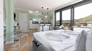 Una habitación de hotel moderna con una cama grande, un balcón con vistas, una kitchenette y un baño.