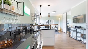 Una cocina moderna con una isla central, un comedor con mesa y sillas, y una sala de estar con sofá y televisor.