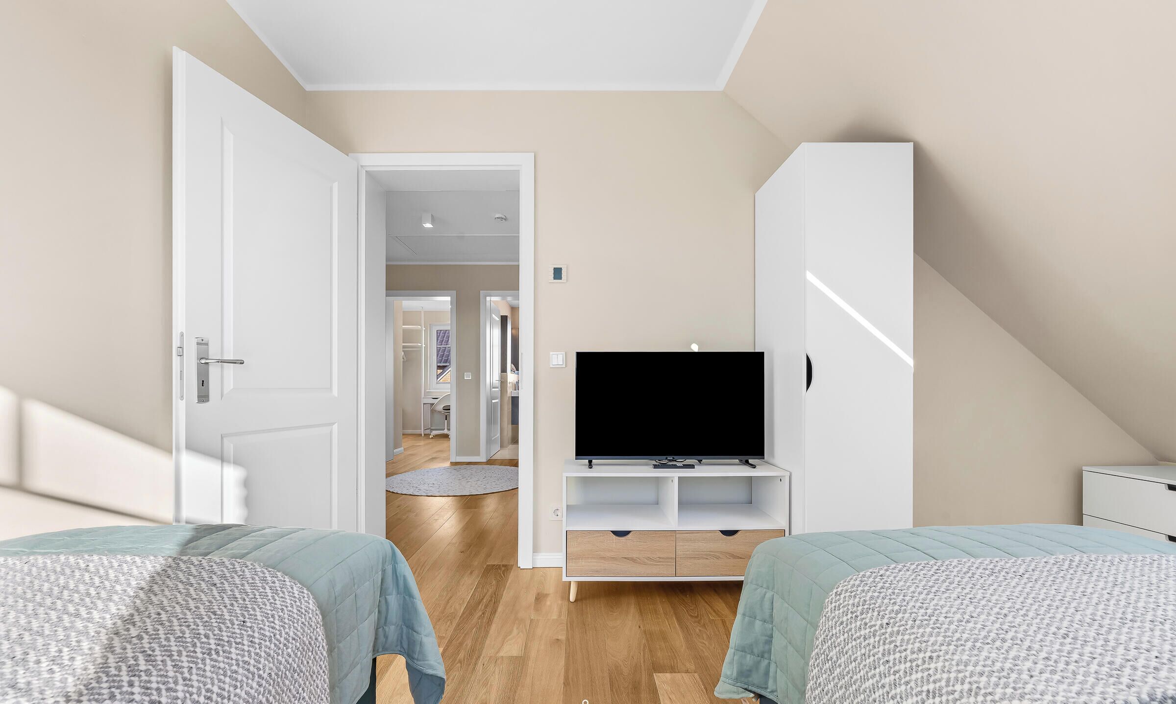 Un dormitorio con televisor, dos camas, un armario y un pasillo que lleva a un baño.