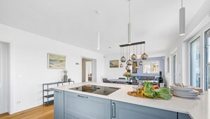 Una cocina moderna con una isla central, iluminación colgante y un comedor con sofá y mesa.