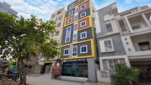 A multi-story RV Grand Hotel with a prominent sign, a tree in front, and a clear sky. - RV Grand (Hyderabad)