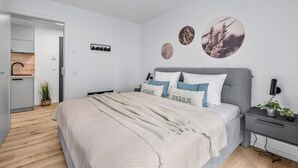 A modern bedroom with a bed, bedside tables, a nightstand, a wall-mounted lamp, and a door leading to another room. - The View C08 Hygge am Deich – Garden Furniture, Parasol, Shared Sauna, Parking (Dagebüll)