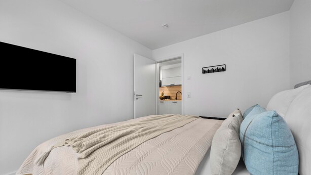 Camera da letto con un letto, una TV a schermo piatto, una porta che conduce al bagno e un quadro raffigurante un panorama urbano.