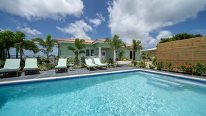 A swimming pool with lounge chairs, a building with a tiled roof, and palm trees. - The View The Ambassador (Jan Thiel)