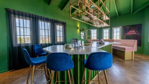 A modern bar area with a green wall, blue bar stools, and a central bar counter. - The View The Ambassador (Jan Thiel)