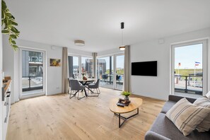 A modern living room with a sofa, a coffee table, and a dining area with chairs and a table. - The View A03 Deichblick - Balcony, garden furniture, elevator, shared Sauna (Dagebüll)