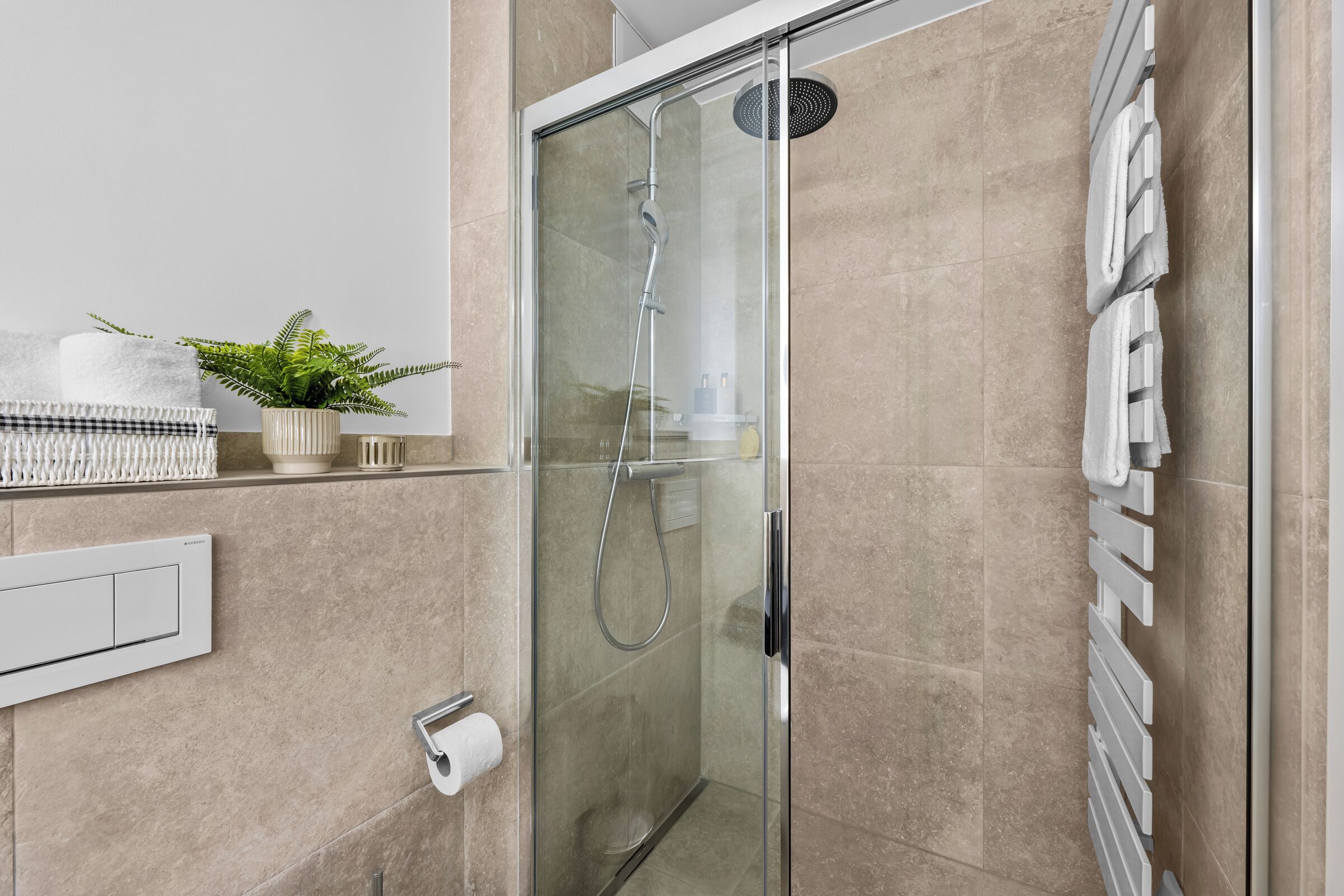 Een moderne badkamer met een douchecabine van glas, een handdoekhouder, een potplant en een toiletrolhouder.