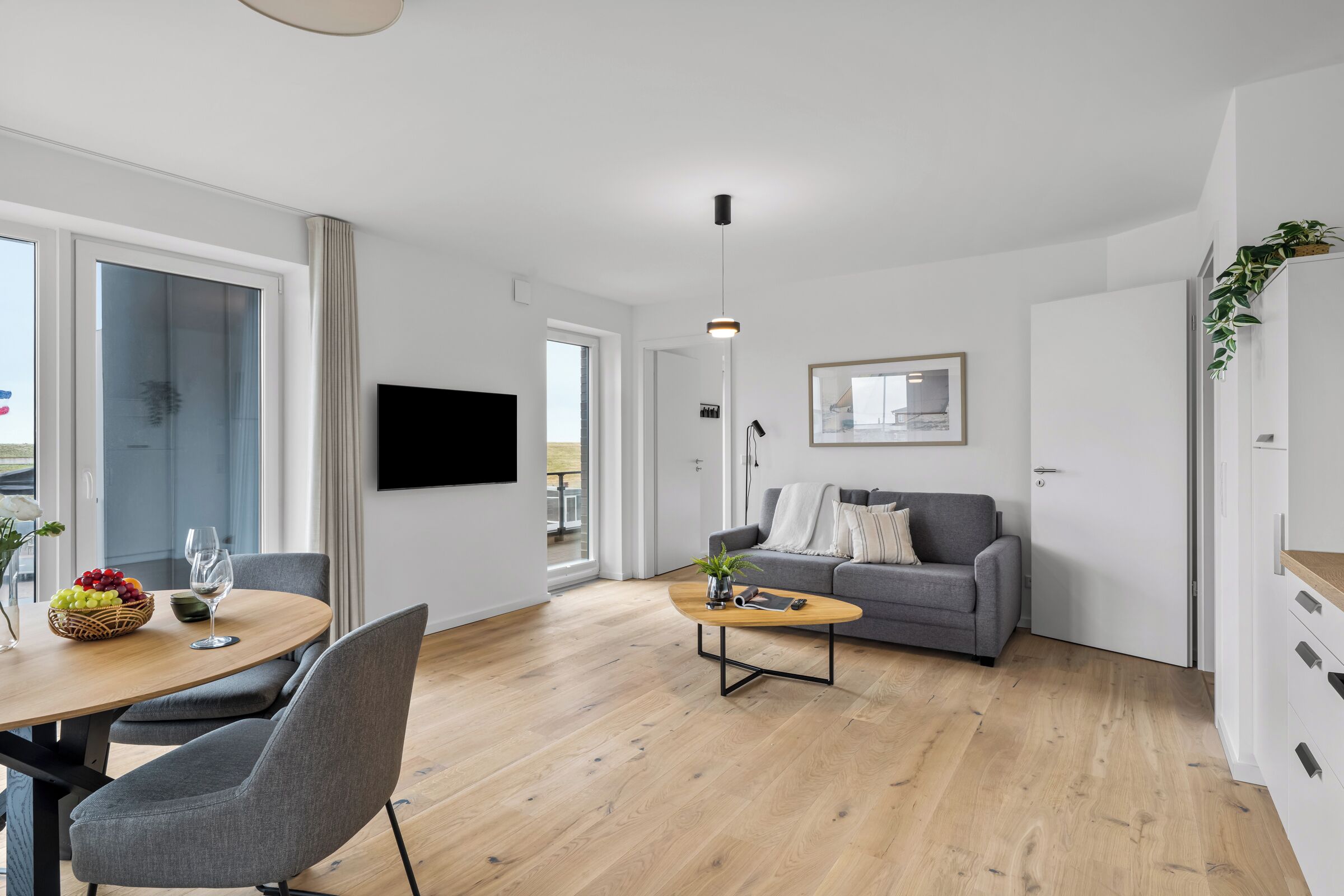 Ett modernt vardagsrum med en grå soffa, ett soffbord i trä och en matplats med ett bord och stolar.