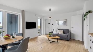 Ett modernt vardagsrum med en grå soffa, ett soffbord i trä och en matplats med ett bord och stolar.