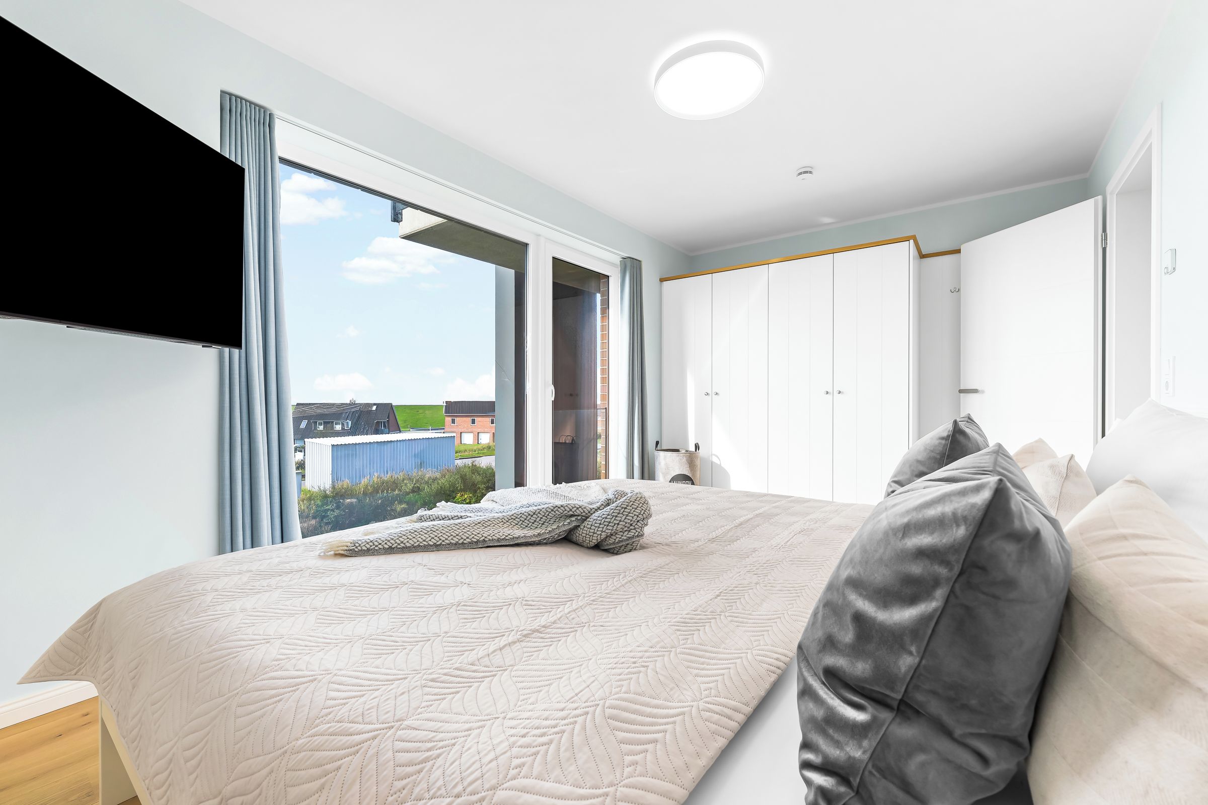 A bedroom with a large bed, a wardrobe, and a window with a view of buildings.