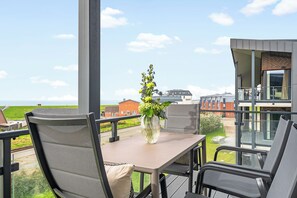 Un balcón con mesa y sillas, un jarrón con flores y vistas al mar y a los edificios.