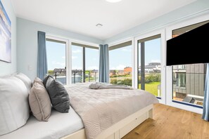 Un dormitorio con una cama grande, un televisor y un balcón con vistas a edificios.