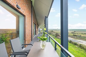 Un balcón con mesa y sillas, un jarrón con flores y vistas al campo.