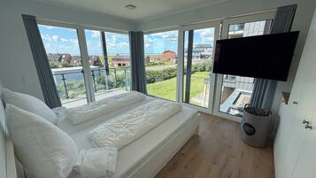 Un dormitorio con una cama grande, un televisor montado en la pared y vistas al exterior.