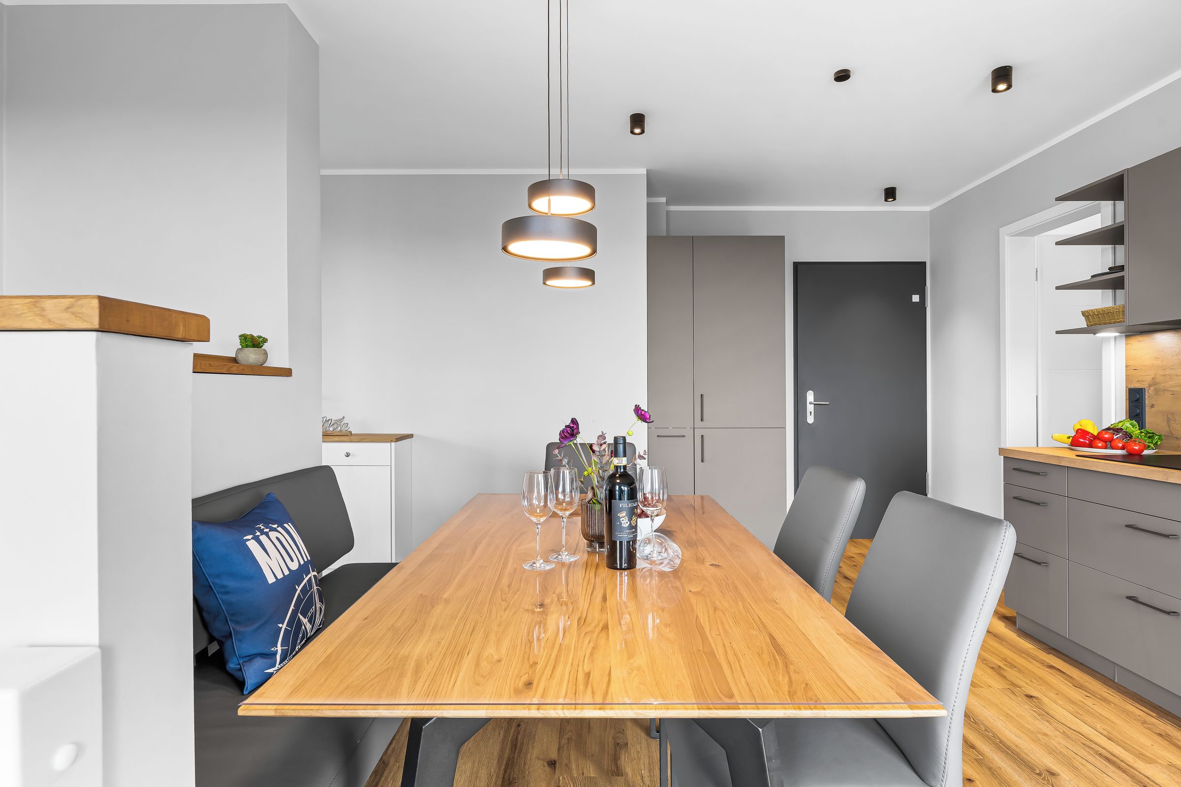 A modern dining area with a wooden table, grey chairs, and pendant lighting.
