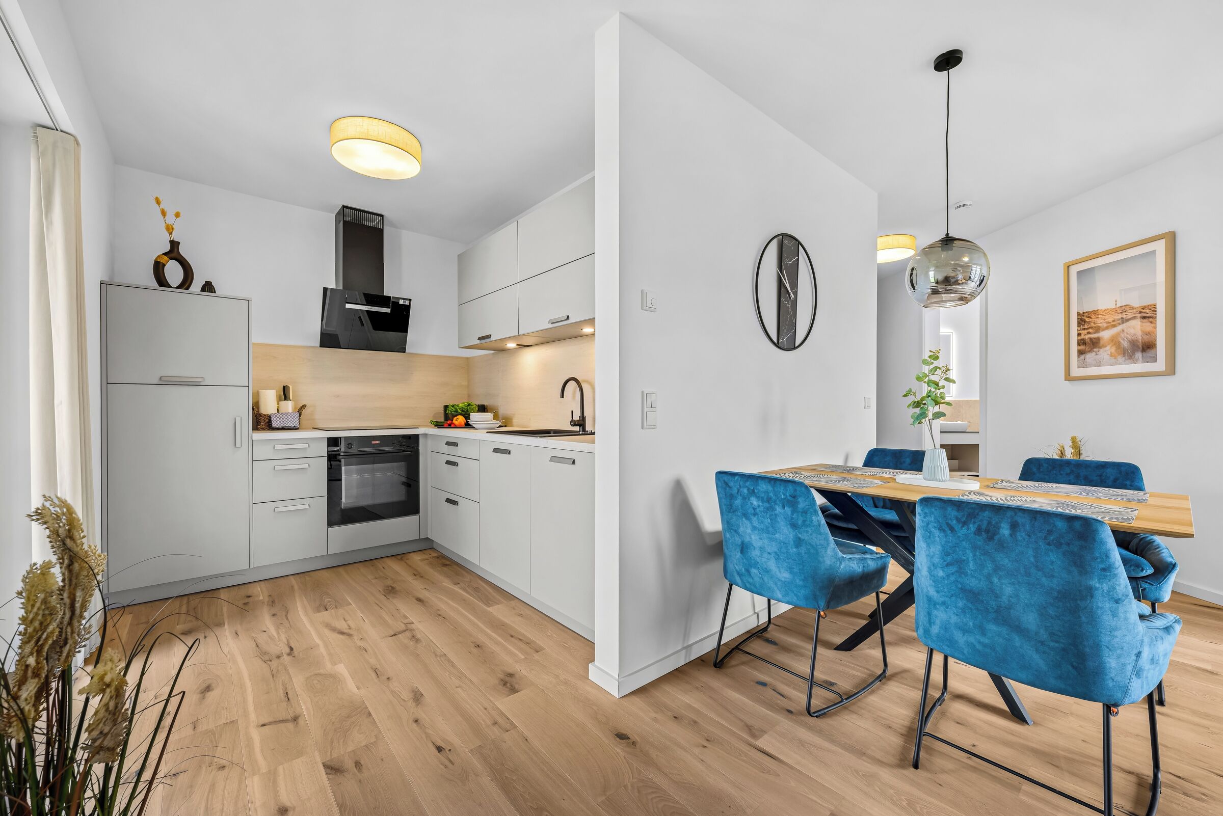 Eine moderne Küche mit weißen Schränken, einem Einbauofen und einem Essbereich mit blauen Stühlen und einem Holztisch.