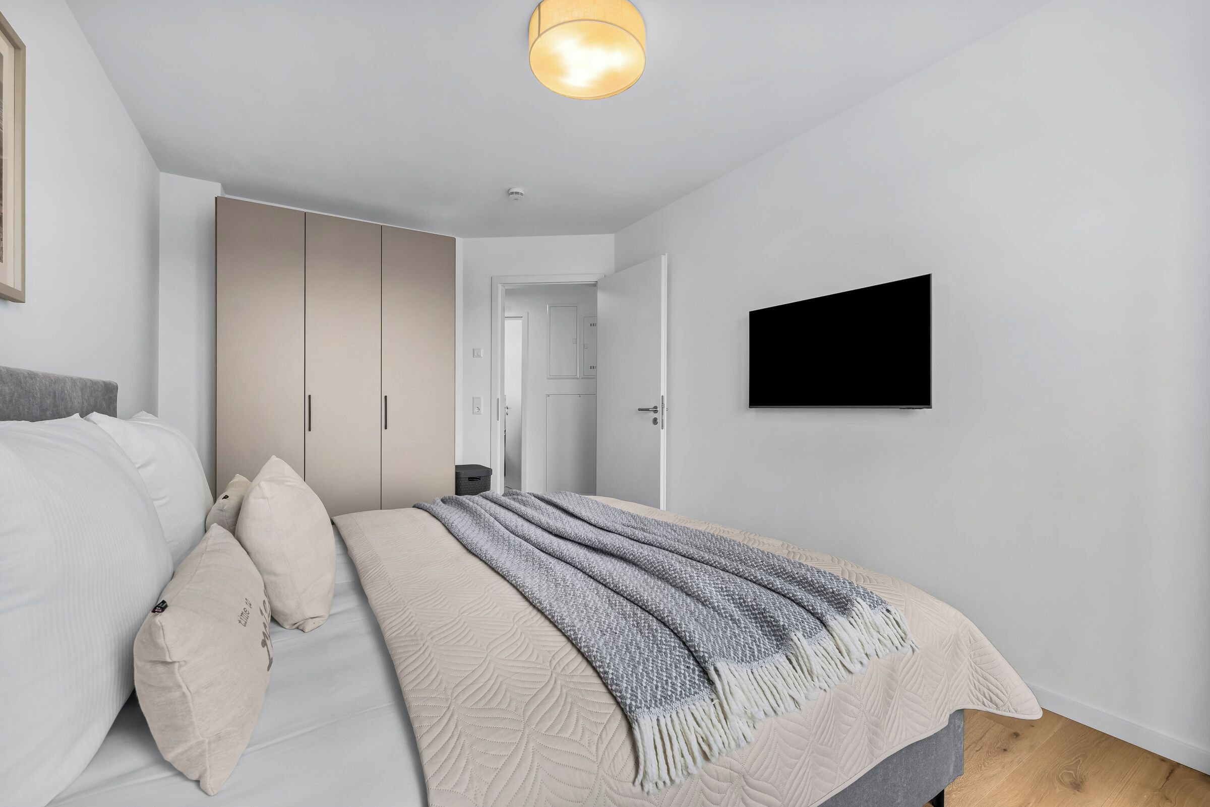 A bedroom with a bed, a wardrobe, a television, and a ceiling light.