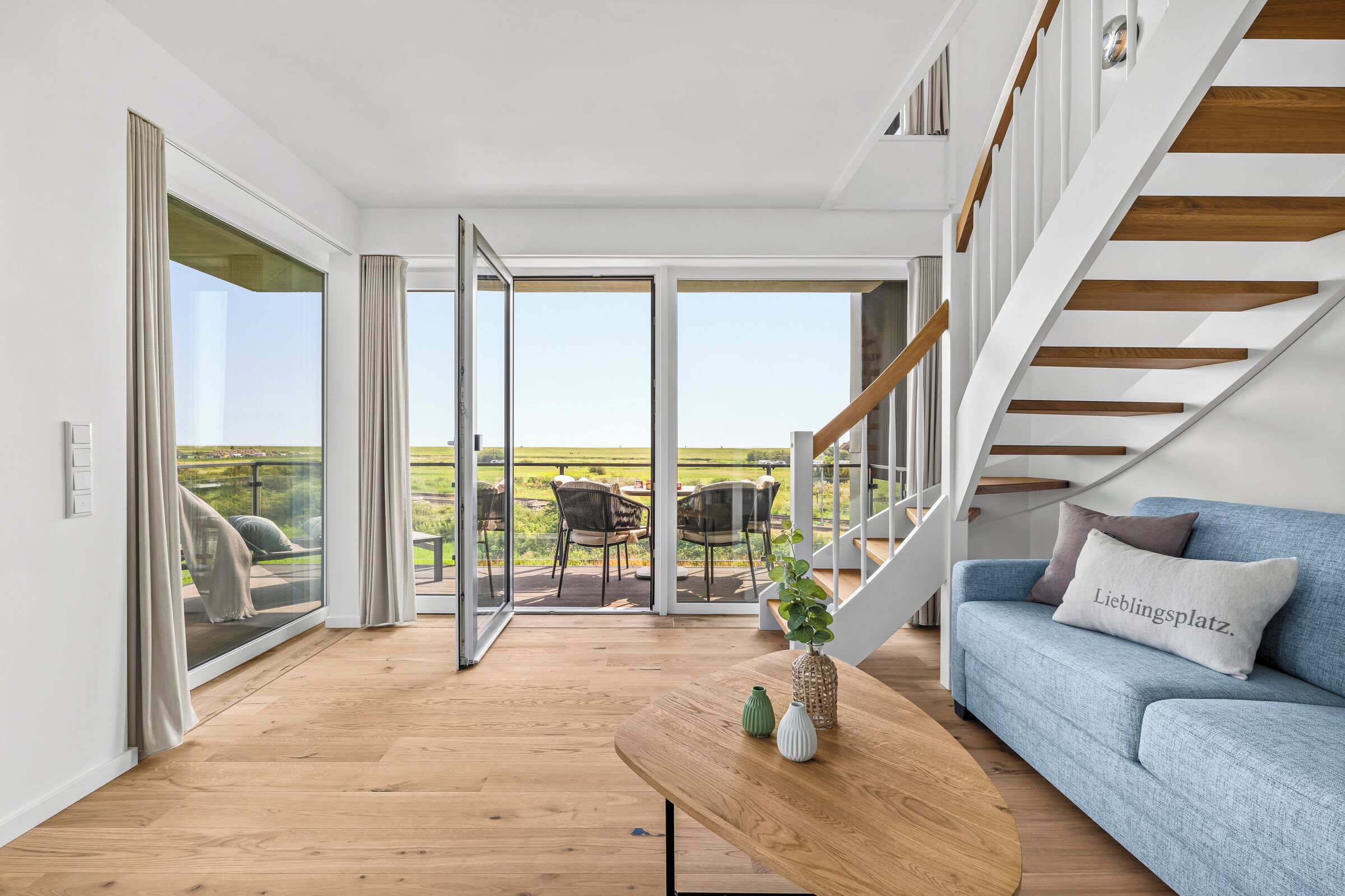A modern living room with a wooden floor, a blue sofa, a coffee table with vases, and a staircase with wooden steps.