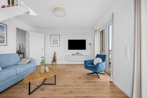 Ein modernes Wohnzimmer mit einem blauen Sofa, einem Holztisch, einem blauen Sessel und einem flachbildfernseher an der Wand.
