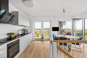 A modern kitchen with a dining area, large windows, and a view of a residential area. - The View C10 Deichkrone - Sauna, shared Washing machine, elevator (Dagebüll)
