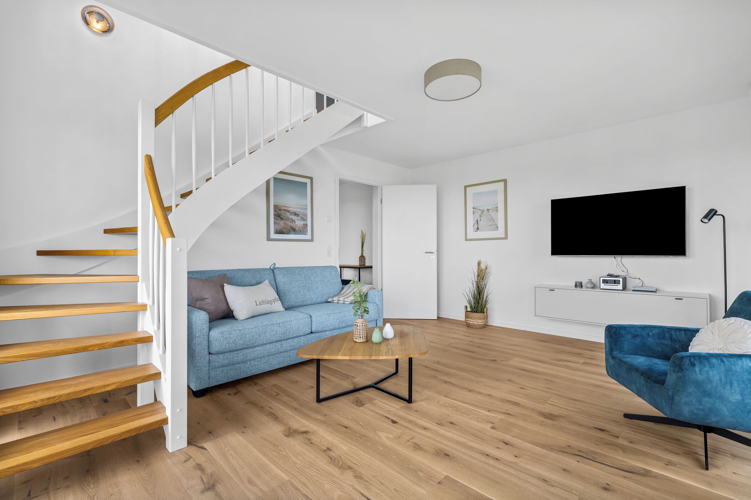 Ein modernes Wohnzimmer mit einer Holztreppe, einem blauen Sofa, einem Couchtisch und einem Flachbildfernseher.
