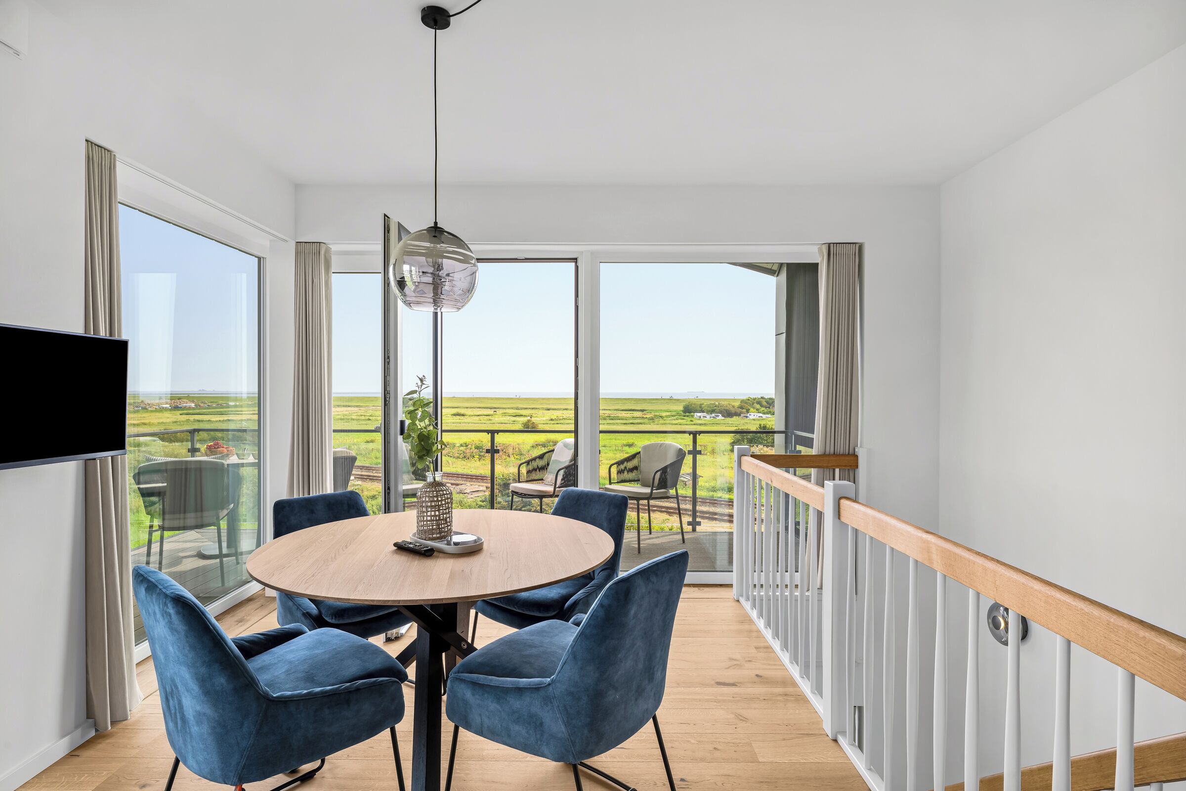 A modern dining area with a round table, blue chairs, and a view of a green landscape through large windows.
