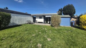 A modern house with a covered patio, a garage, and a well-maintained lawn. - ERNST vacation home close to the Frisian beach in Tossens for the whole family (Butjadingen-Tossens)