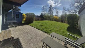 A covered patio with a grassy lawn, a blue building, and a clear sky. - ERNST vacation home close to the Frisian beach in Tossens for the whole family (Butjadingen-Tossens)