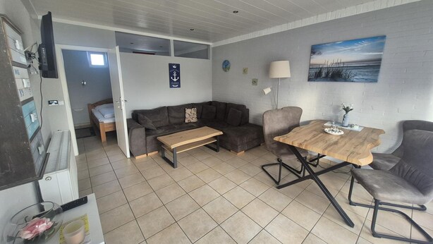 A compact living space with a sofa, a dining table, a lamp, and a painting on the wall. - ERNST vacation home close to the Frisian beach in Tossens for the whole family (Butjadingen-Tossens)