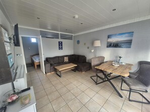 A compact living space with a sofa, a dining table, a lamp, and a painting on the wall. - ERNST vacation home close to the Frisian beach in Tossens for the whole family (Butjadingen-Tossens)