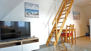 Un salon moderne avec un téléviseur, une échelle en bois et des œuvres d’art accrochées aux murs.