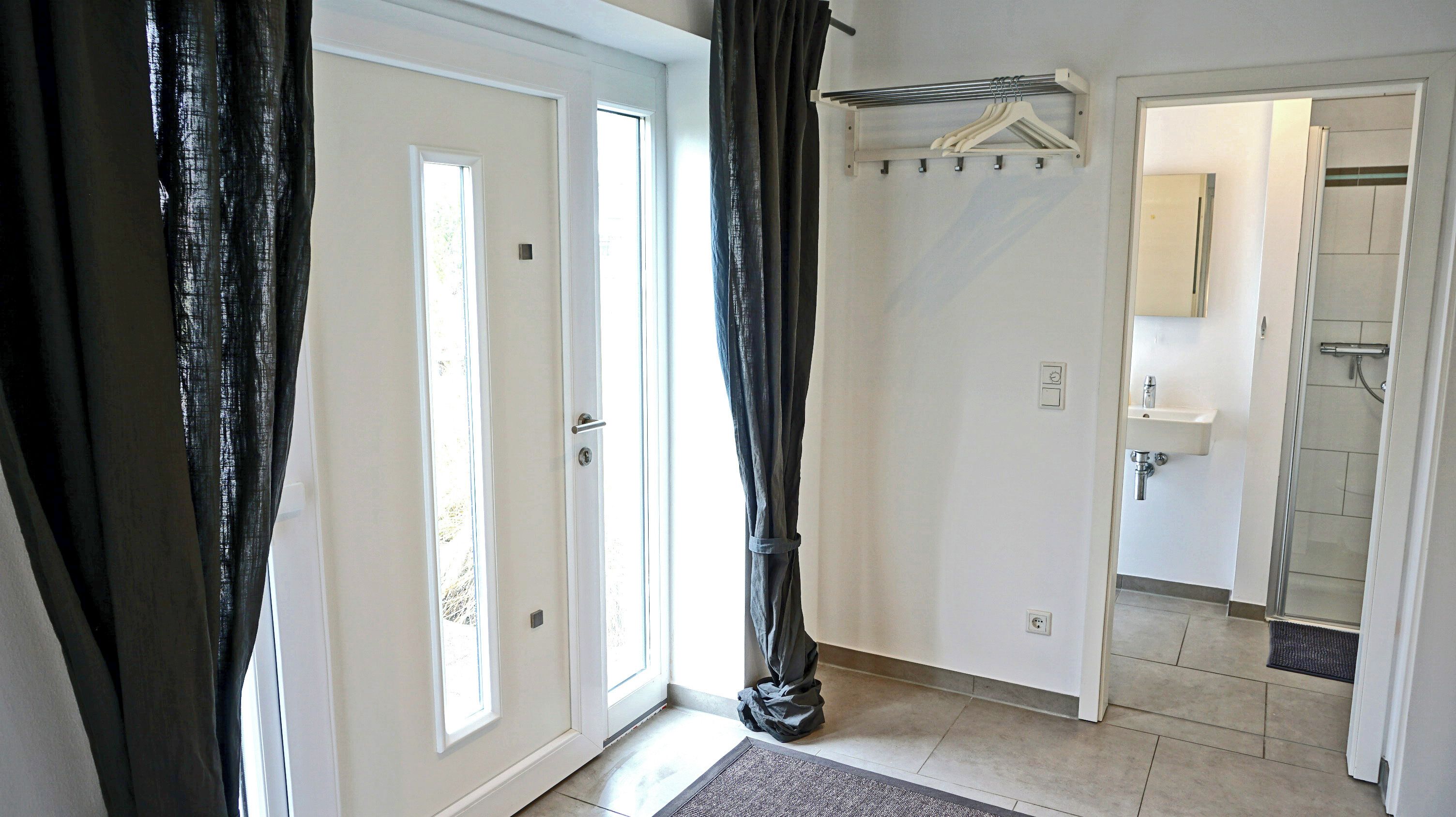 A hotel room with a door, a coat rack, a shower, and a bathroom.