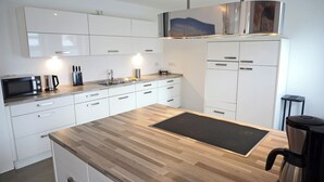 Moderni keittiö, jossa on valkoiset kaapit, sisäänrakennettu mikroaaltouuni, vedenkeitin ja kahvinkeitin.