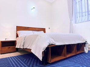 Une chambre à coucher avec un cadre de lit en bois, du linge de lit blanc, une table de chevet avec une lampe et un tapis bleu.