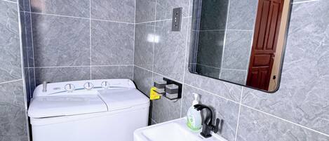 A bathroom with a white washing machine, a sink with a mirror above it, and a toilet.