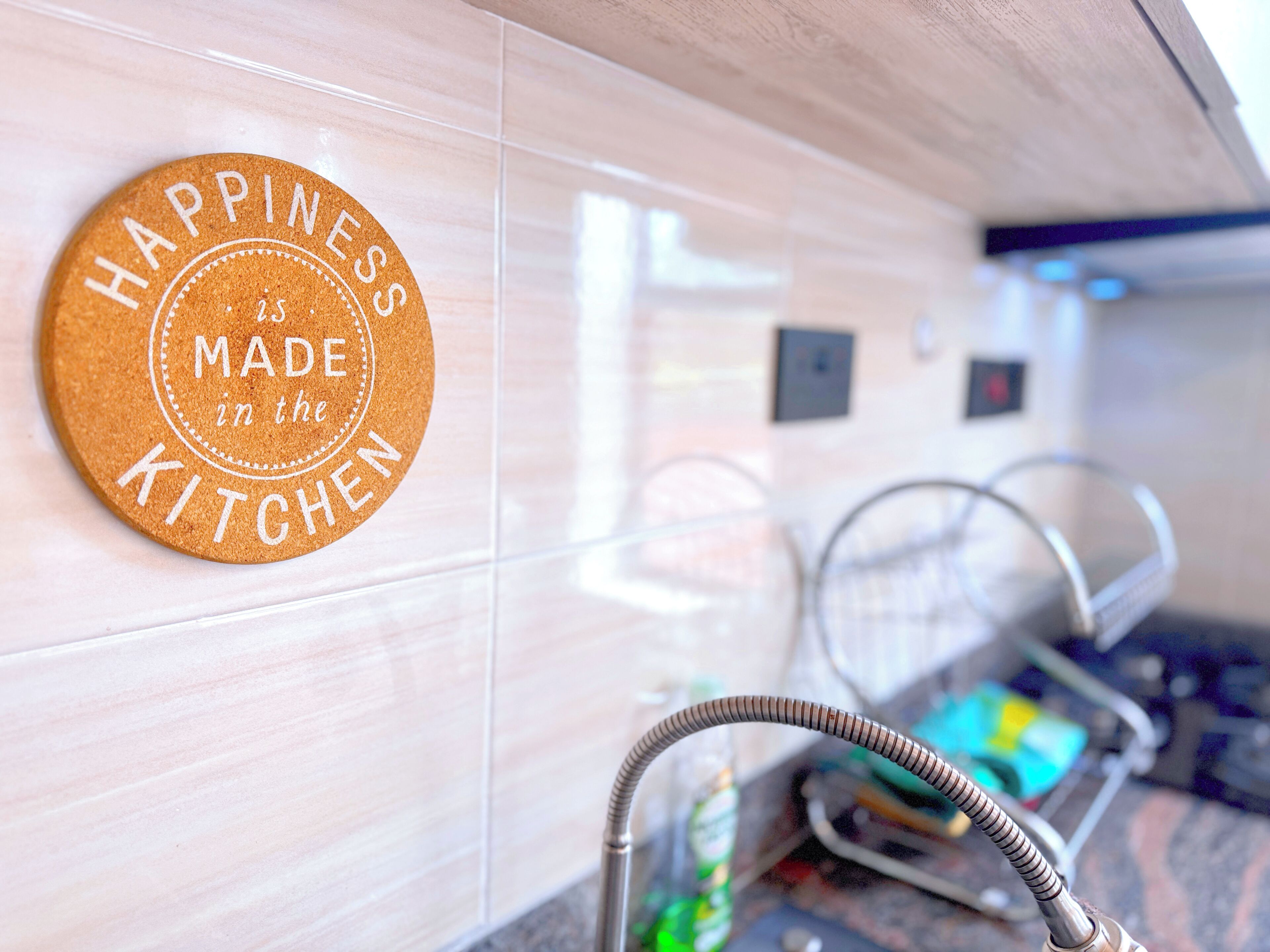 A cork placemat with the text 'HAPPINESS is MADE in the KITCHEN' on a tiled wall.