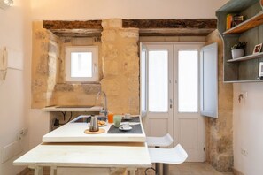 Eine kleine Küche mit einer Steinwand, einem Fenster und einem Holzregal mit Büchern.