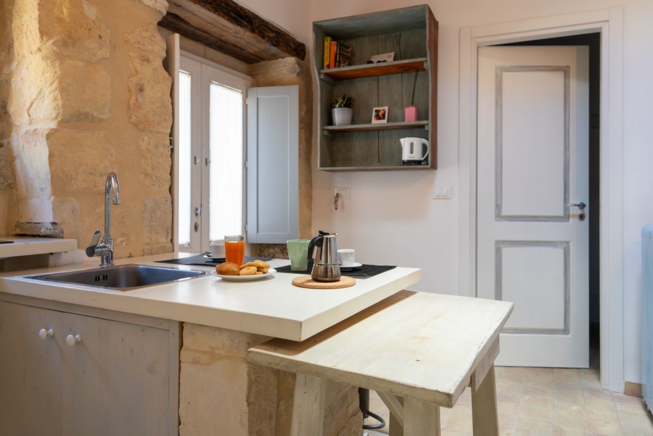 Una cocina con pileta, espacio para desayunar, estante con libros y tetera, además de una puerta.