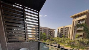 Un balcon offrant une vue sur des immeubles modernes, doté d’une balustrade en verre et de deux chaises grises.