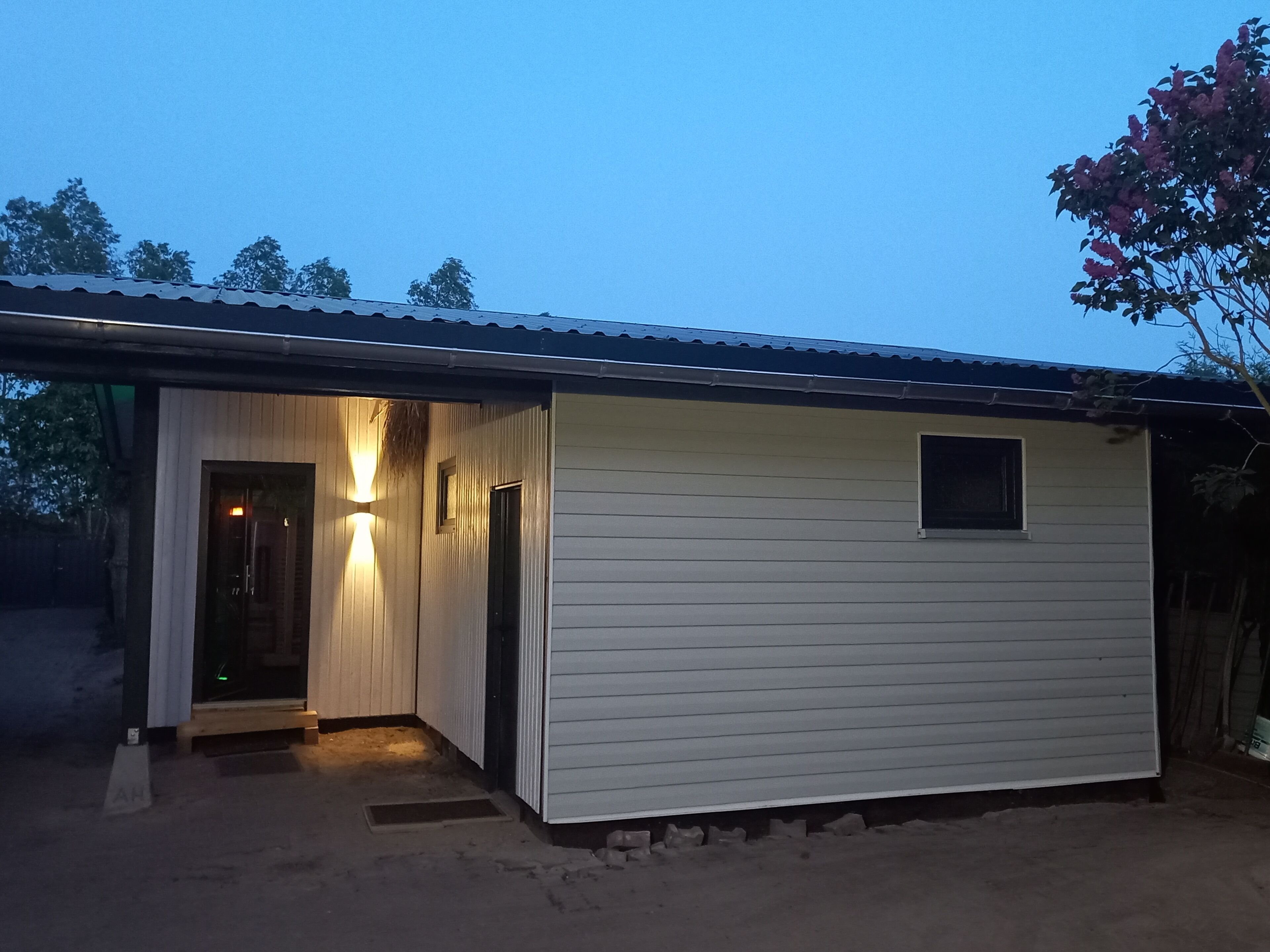 Een laag gebouw met een schuin dak, een klein raam en een deur die naar een binnenruimte leidt.