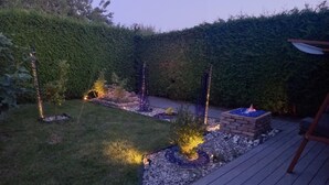 A landscaped garden with a fire pit, decorative lights, and a wooden deck.