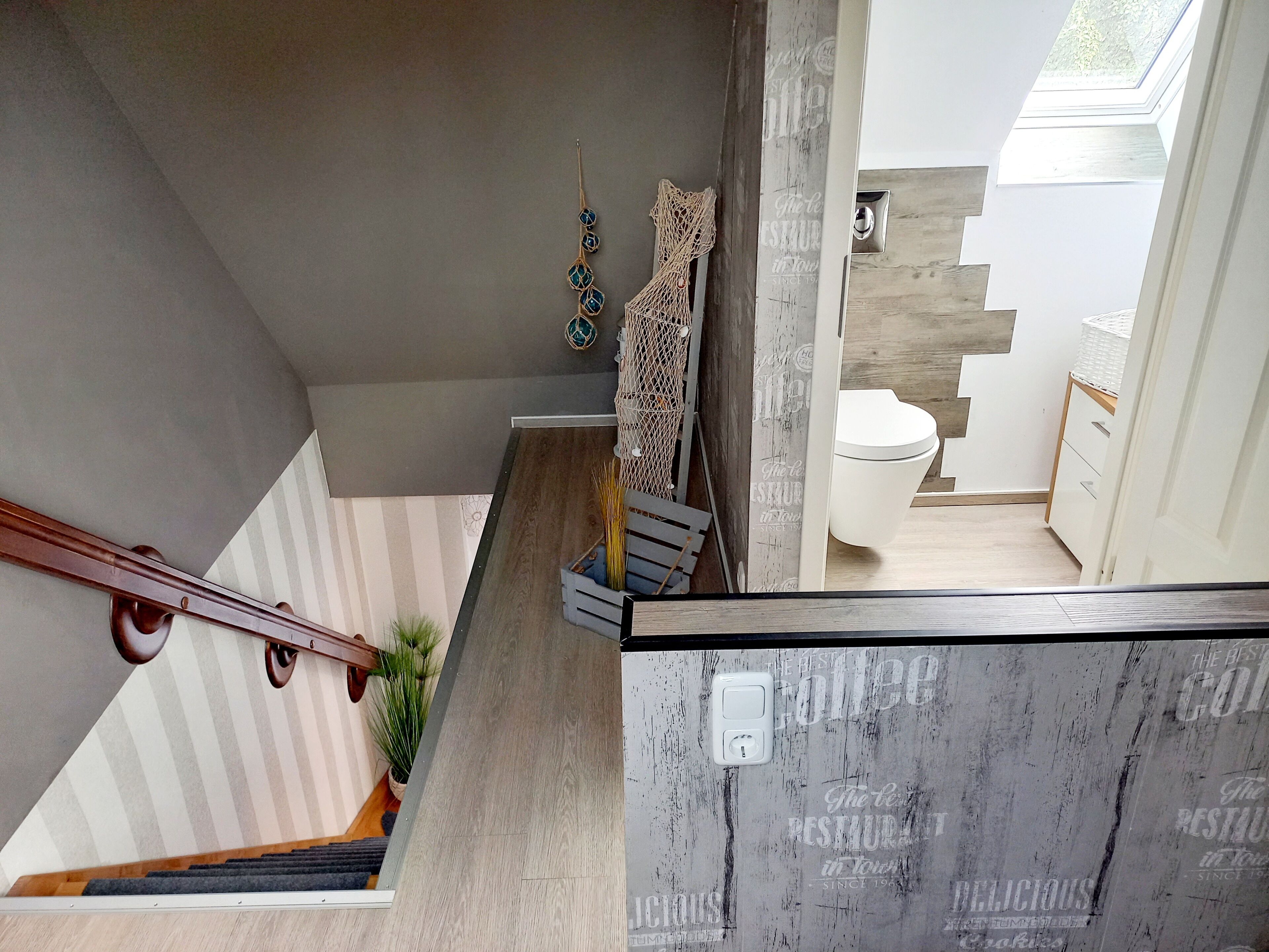 Un interior modern amb una escala, una paret de fusta, un vàter blanc i una petita cuina.