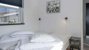 A bedroom with a bed, bedside lamps, a small table, and a window with blinds. - 4 Star Holiday Home in Juelsminde (Juelsminde)